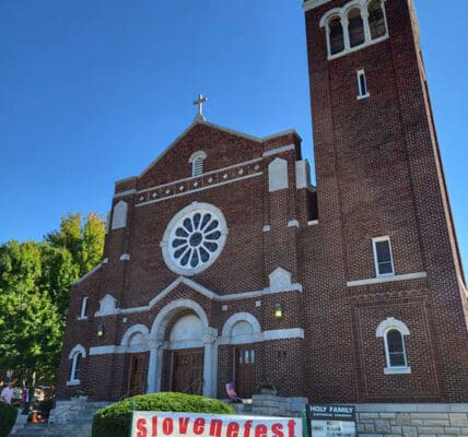 exterior of holy family parish, kansas, a large red brick building with white trim on a bright sunny cloudless day