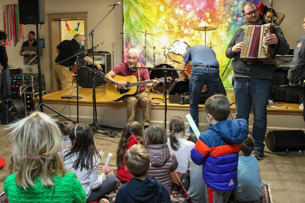 a group of men playing guitar and accordian to a group of young children at the Slovenian National home