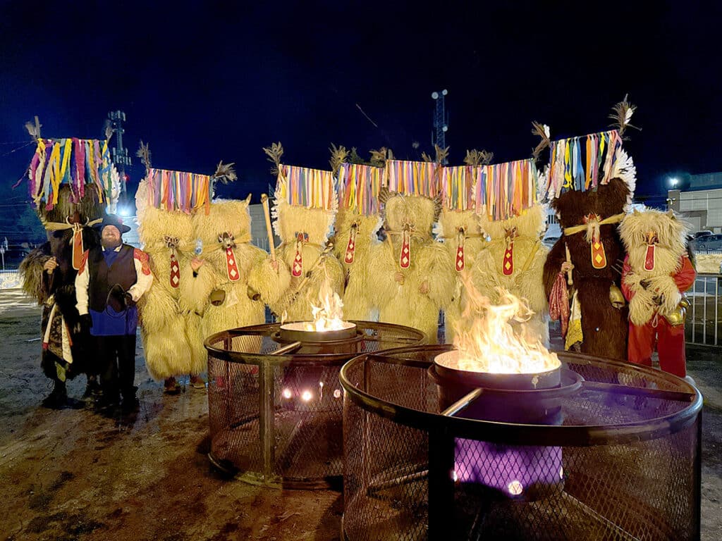 a group of Kurenti around some firepits at night time