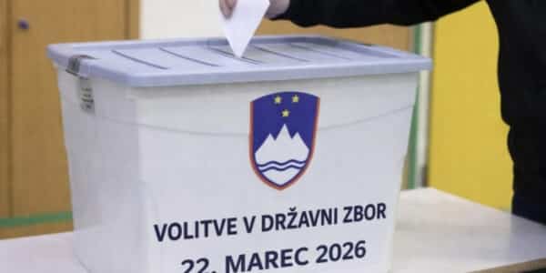 a hand placing a voting ballot into a collection box