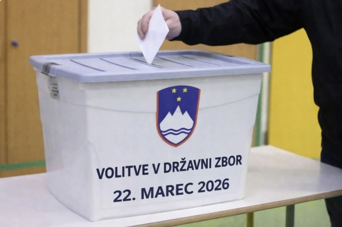 a hand placing a voting ballot into a collection box