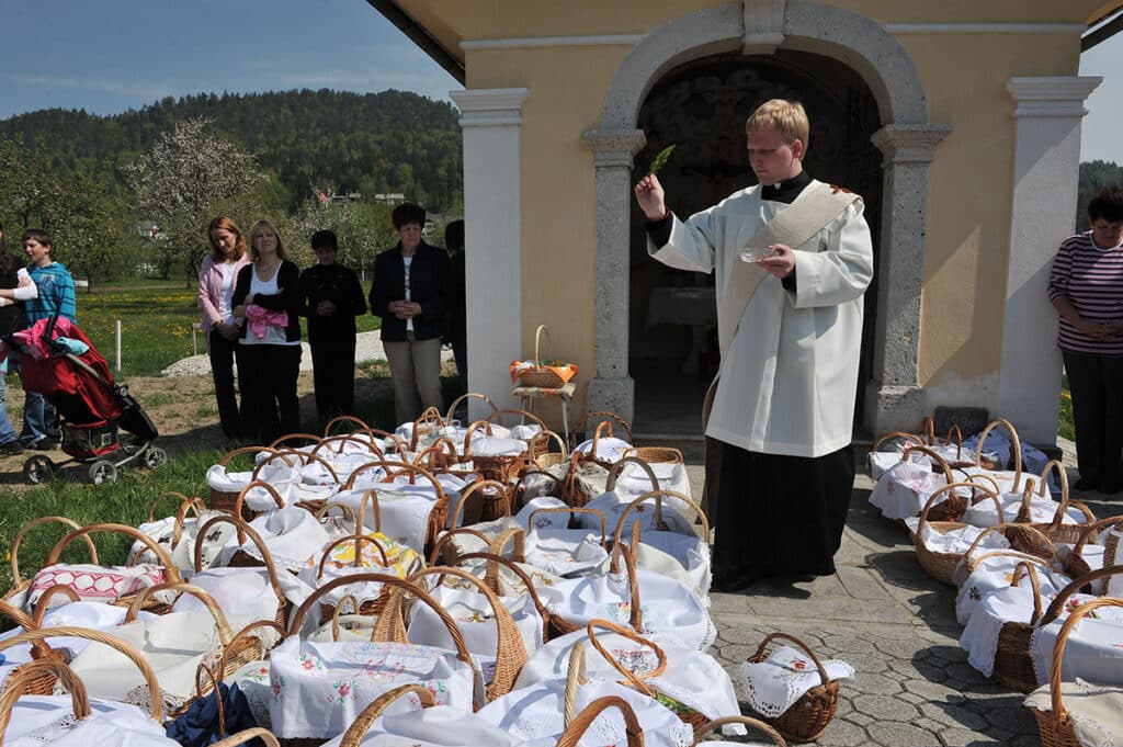 priest blessing food baskets outside of church on a sunny holy saturday