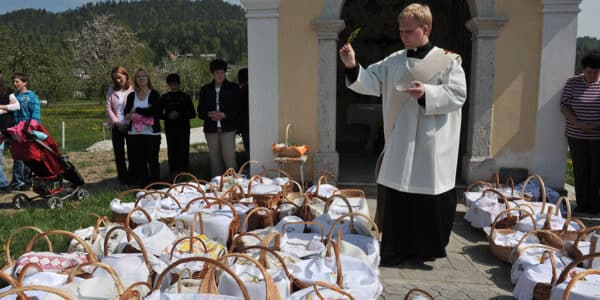priest blessing food baskets outside of church on a sunny holy saturday