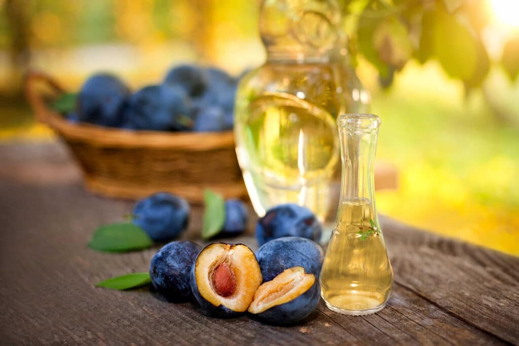several cut plums in front of glass bottles on a picnic table