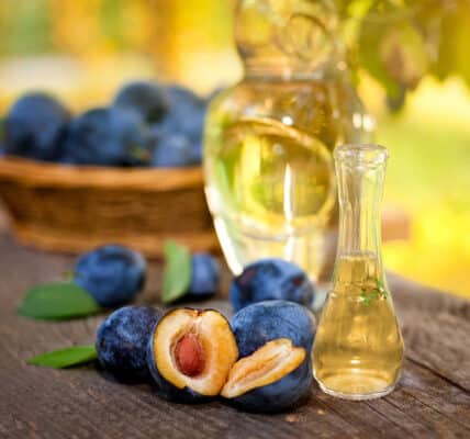 several cut plums in front of glass bottles on a picnic table