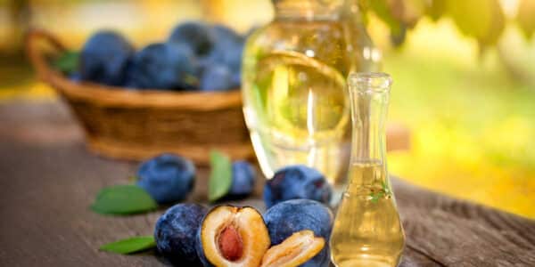 several cut plums in front of glass bottles on a picnic table