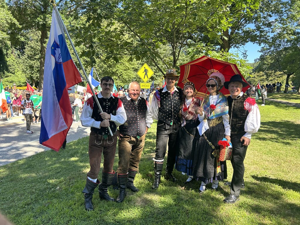group of people dressed in traditional slovenian costumes with flags and umbrellas wait to march in the parade