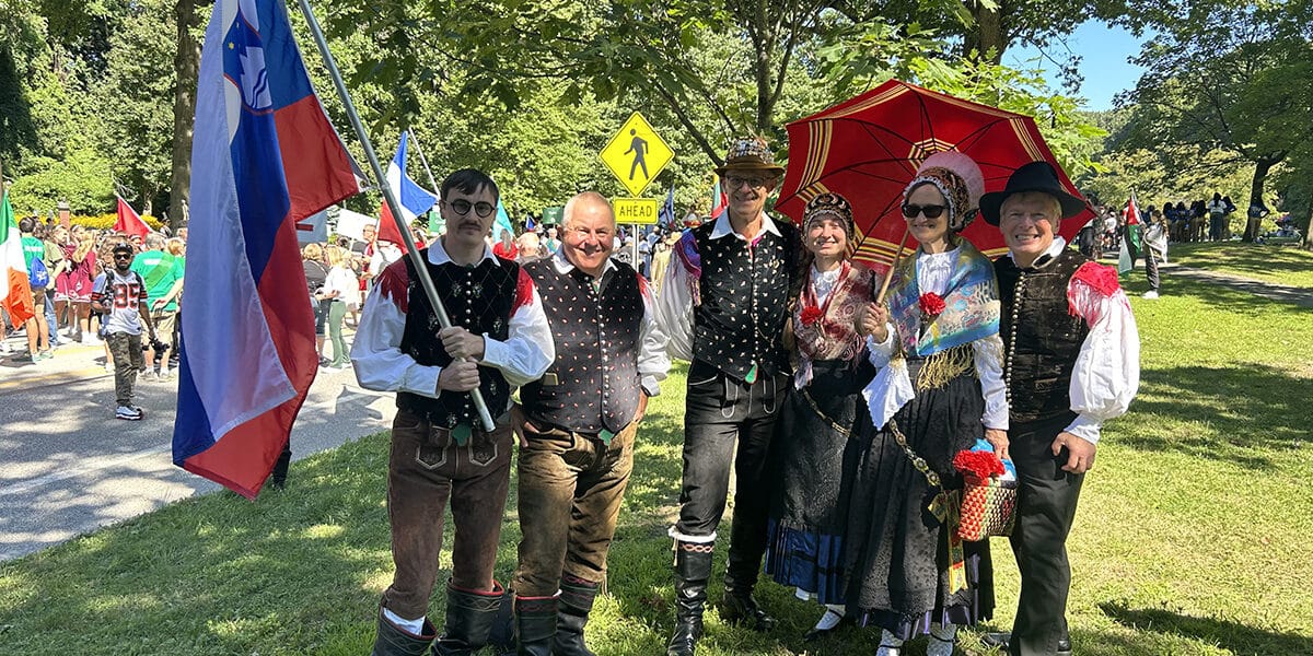 group of people dressed in traditional slovenian costumes with flags and umbrellas wait to march in the parade