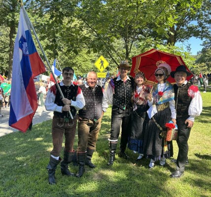 group of people dressed in traditional slovenian costumes with flags and umbrellas wait to march in the parade
