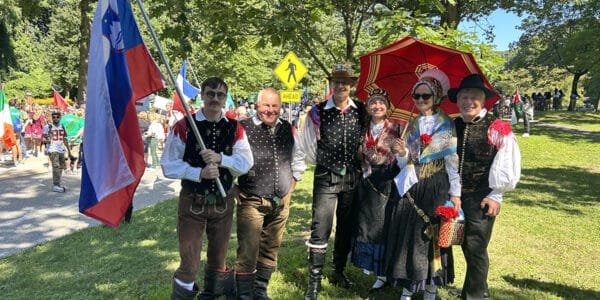 group of people dressed in traditional slovenian costumes with flags and umbrellas wait to march in the parade